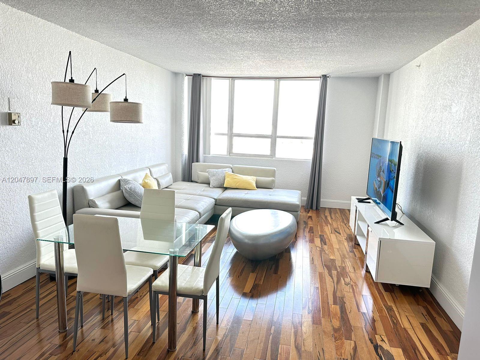 A living and dining area features a sectional sofa, glass table, and hardwood flooring — 1500 Bay Rd # 1408S, Miami Beach FL 33139, MIAMI BEACH, FL