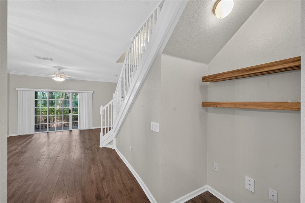 An empty room with wood-look flooring, a dining chandelier, a ceiling fan, and a staircase — 5008 NW 44TH LANE UNIT 102, GAINESVILLE, FL