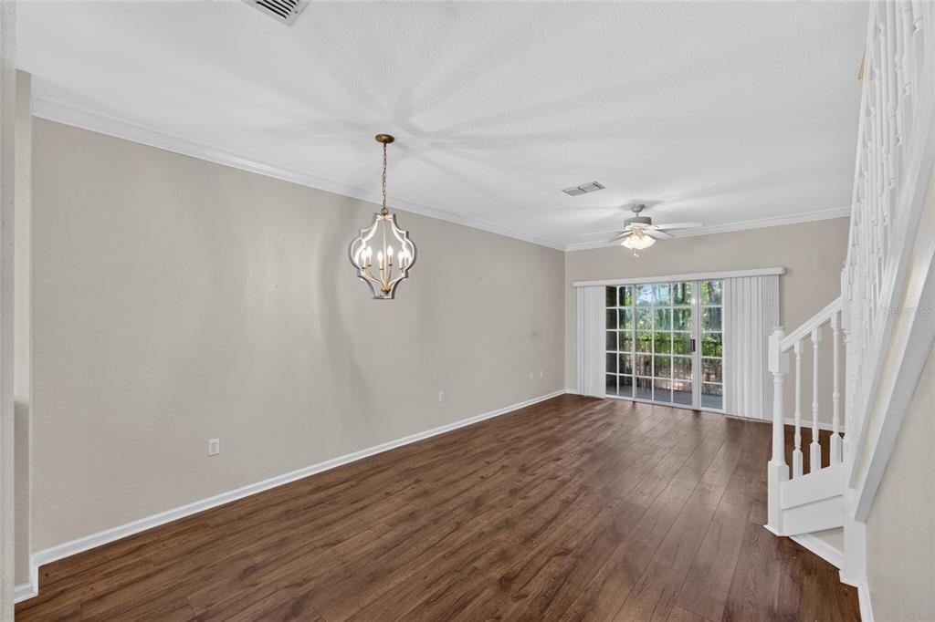 A living room features wood-look flooring, a white staircase, a decorative chandelier, and sliding glass doors — 5008 NW 44TH LANE UNIT 102, GAINESVILLE, FL
