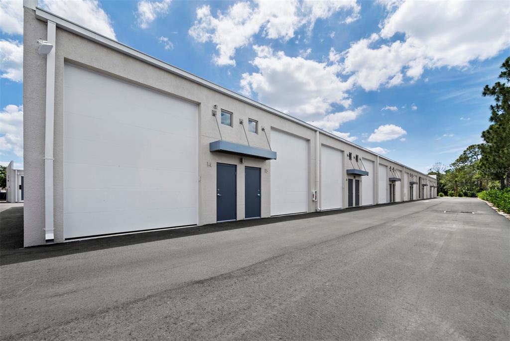 An exterior view of a commercial warehouse building with multiple roll-up doors and entry doors — 829 57TH STREET E UNIT 14, BRADENTON, FL