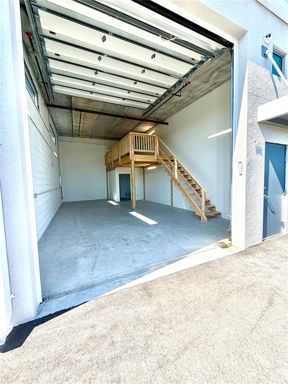 An open warehouse unit features a concrete floor, a roll-up door, and a wooden mezzanine — 829 57TH STREET E UNIT 14, BRADENTON, FL