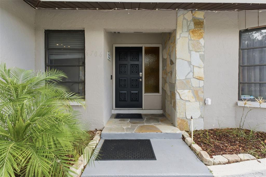 The front entrance features a black door, stone siding, and a concrete walkway — 6706 WALDORF COURT, NEW PORT RICHEY, FL