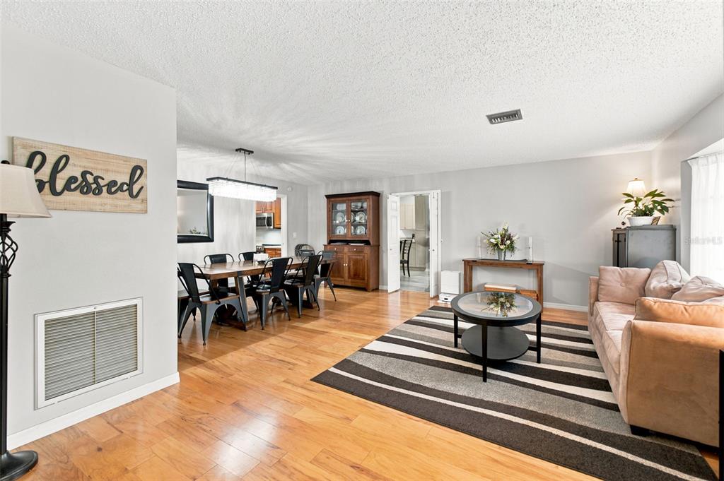 An open-concept living and dining area features hardwood floors, a striped rug, and neutral walls — 6706 WALDORF COURT, NEW PORT RICHEY, FL