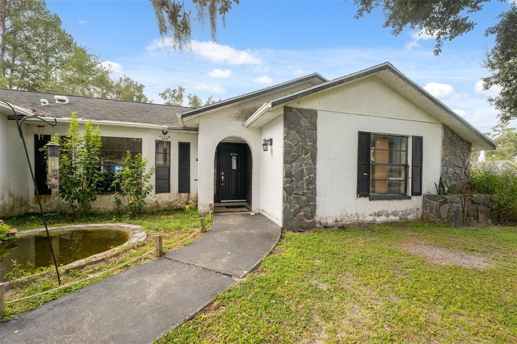 A single-story house with white stucco, stone accents, a black front door, and a pond — 18160 SPANGLER AVENUE, BROOKSVILLE, FL