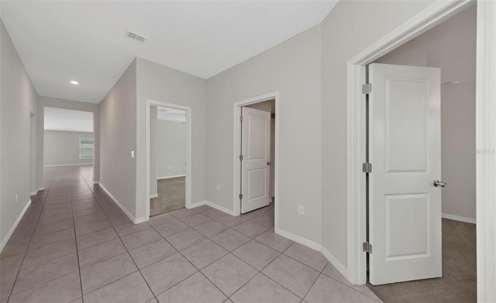 A hallway with light gray walls and tiled floors leads to several open doorways — 16612 CARLTON POND STREET, WIMAUMA, FL