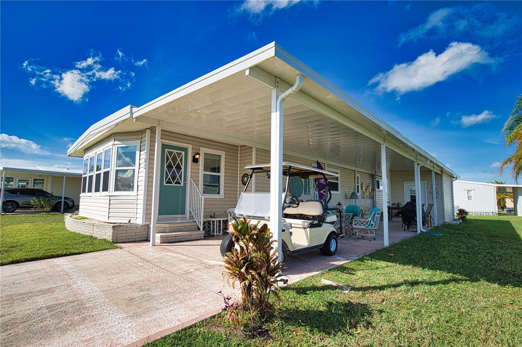 A manufactured home features a large covered carport, a golf cart, and a concrete driveway — 702 BLANCA, NORTH PORT, FL