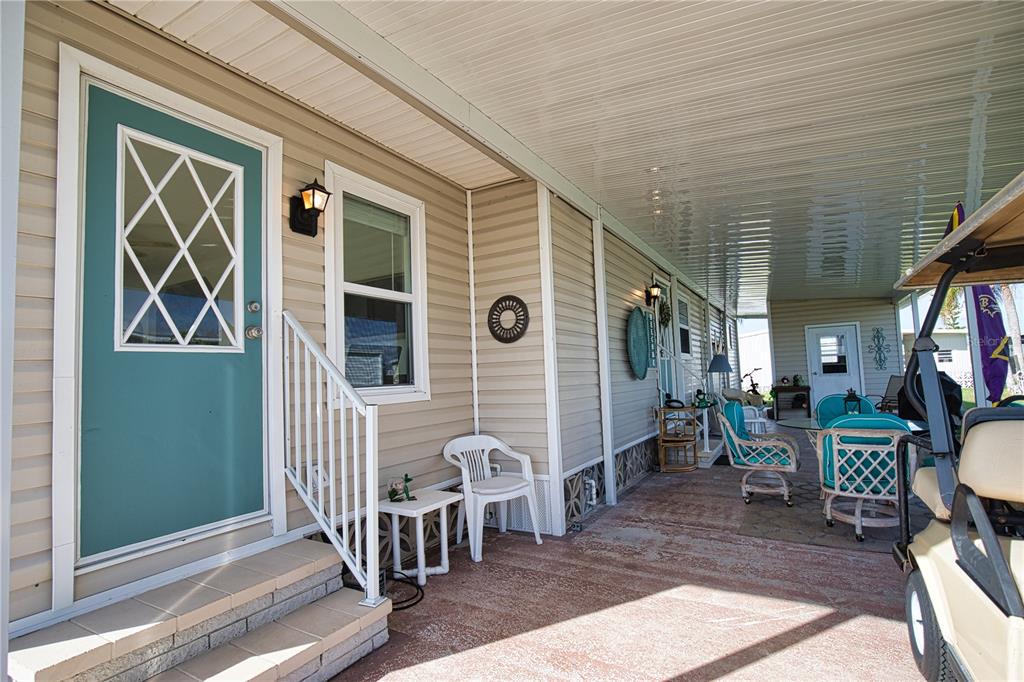 A covered patio features a teal front door, outdoor furniture, and a parked golf cart — 702 BLANCA, NORTH PORT, FL