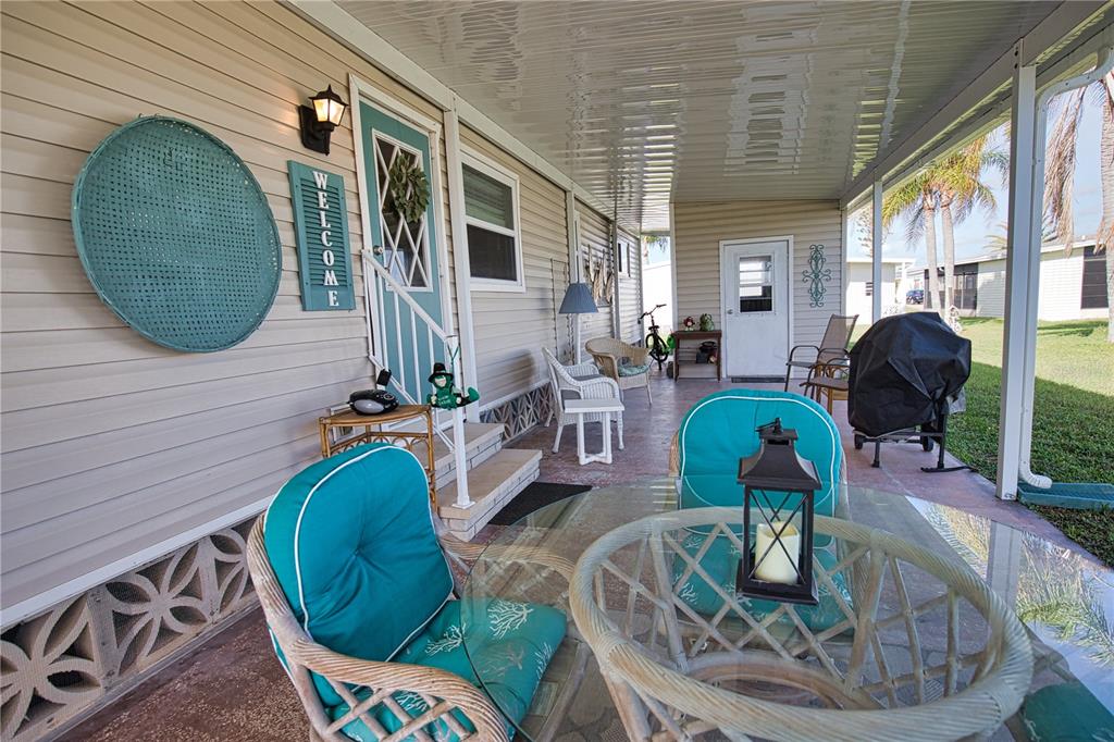 A covered patio features wicker furniture, a glass-top table, and a teal welcome sign — 702 BLANCA, NORTH PORT, FL