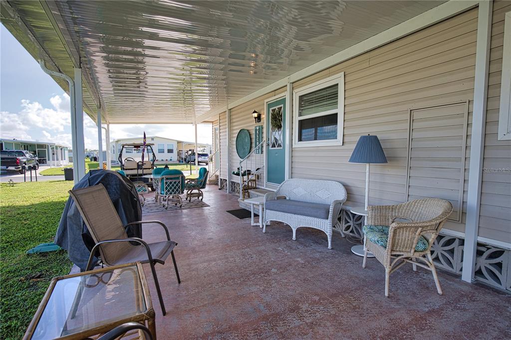 A covered patio features wicker furniture, a small table, and a view of a golf cart — 702 BLANCA, NORTH PORT, FL