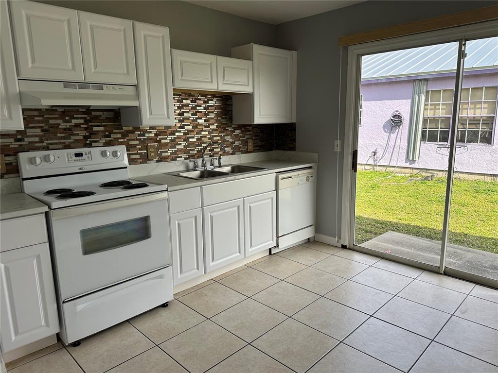 A kitchen features white cabinets, a mosaic tile backsplash, white appliances, and a sliding glass door — 425 RICOLD TERRACE, PORT CHARLOTTE, FL