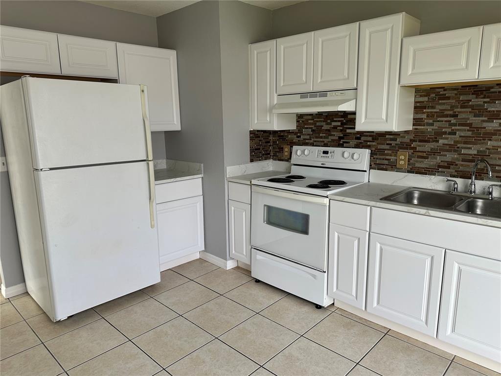 A kitchen features white cabinets, white appliances, a tiled backsplash, and light-colored floor tiles — 425 RICOLD TERRACE, PORT CHARLOTTE, FL