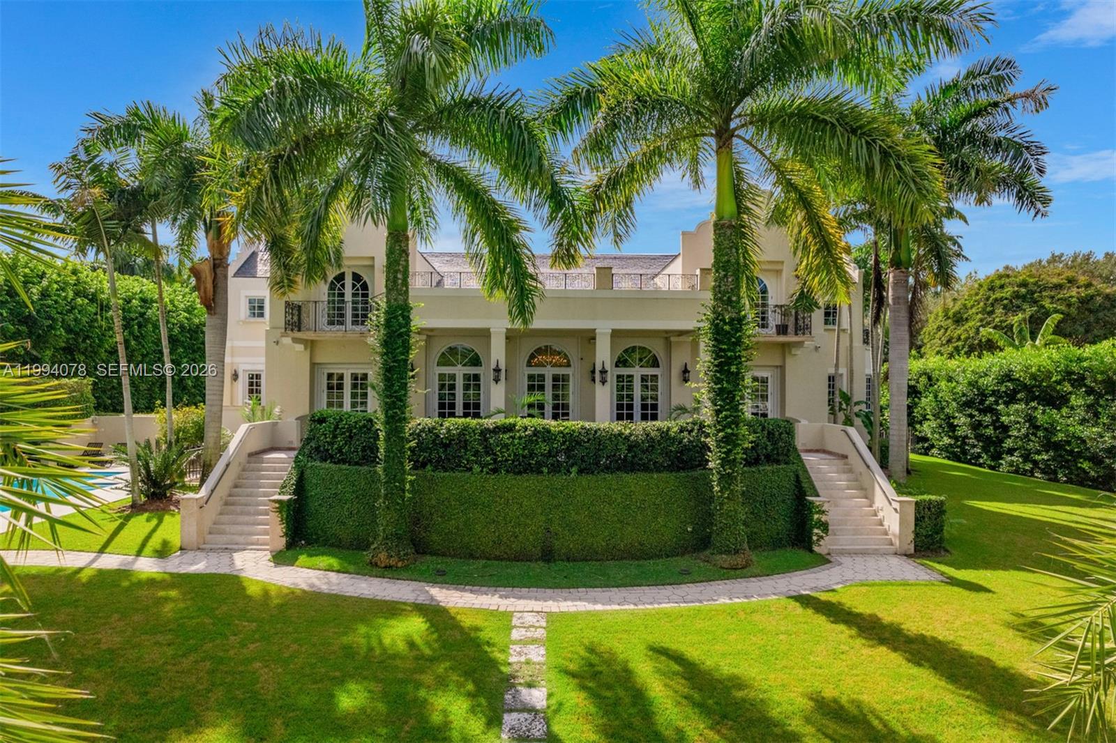 A large two-story house features a manicured hedge, twin staircases, and tall palm trees — 585 Arvida Pkwy, Coral Gables FL 33156, CORAL GABLES, FL