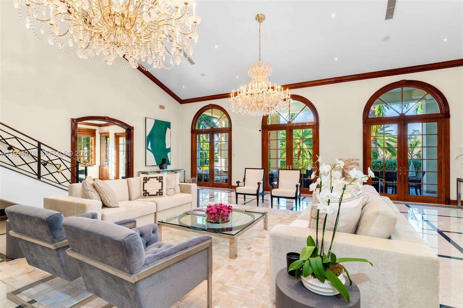 A spacious living room features two crystal chandeliers, arched glass doors, and light-colored furniture — 585 Arvida Pkwy, Coral Gables FL 33156, CORAL GABLES, FL