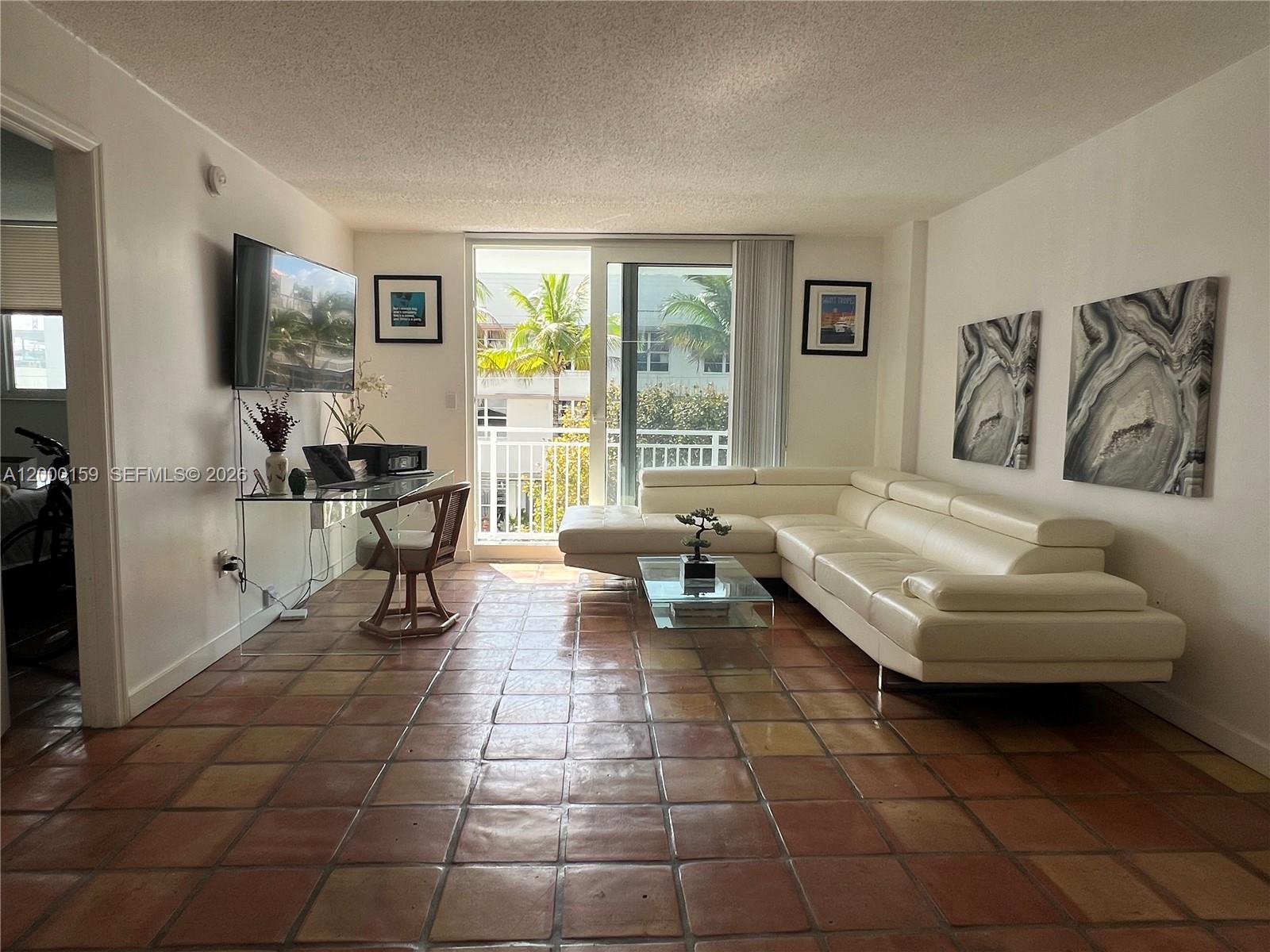 A living room features a white sectional sofa, glass desk, and terracotta tile flooring — 345 Ocean Dr # 303, Miami Beach FL 33139, MIAMI BEACH, FL