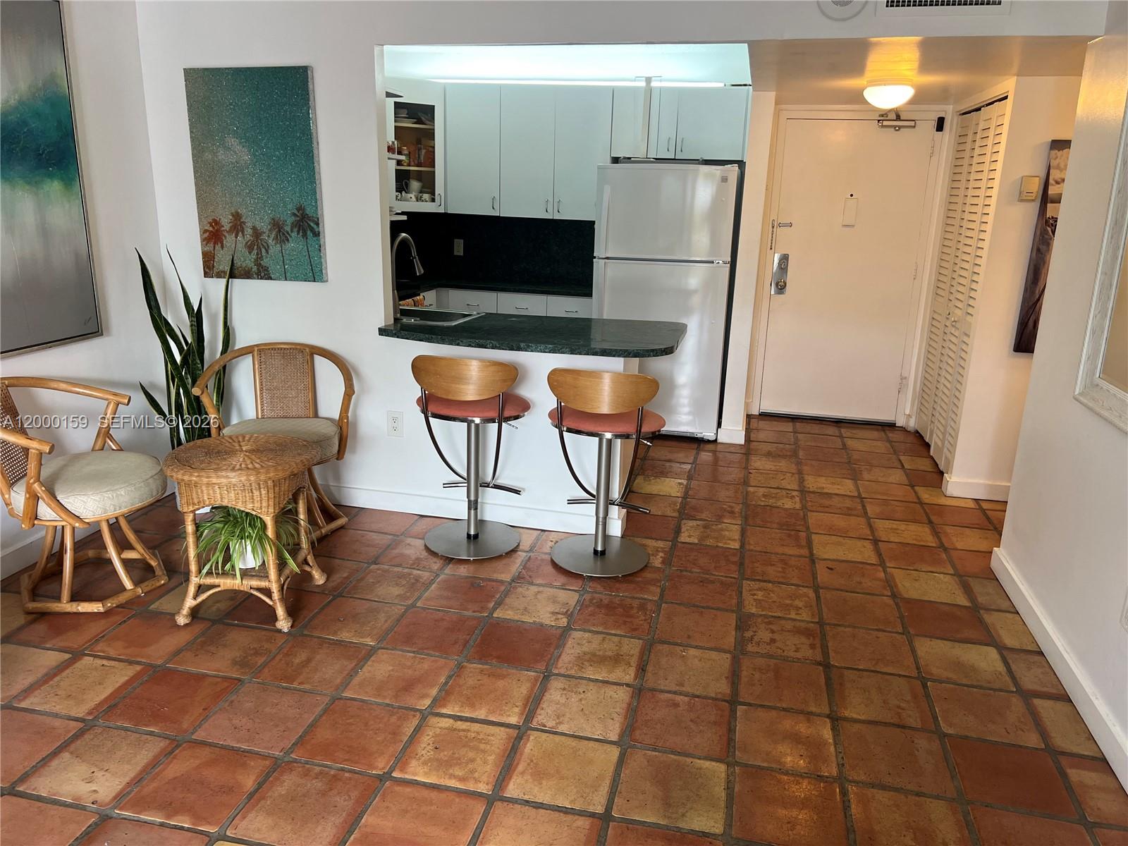 A kitchen with white cabinets and a breakfast bar opens into a tiled living area — 345 Ocean Dr # 303, Miami Beach FL 33139, MIAMI BEACH, FL