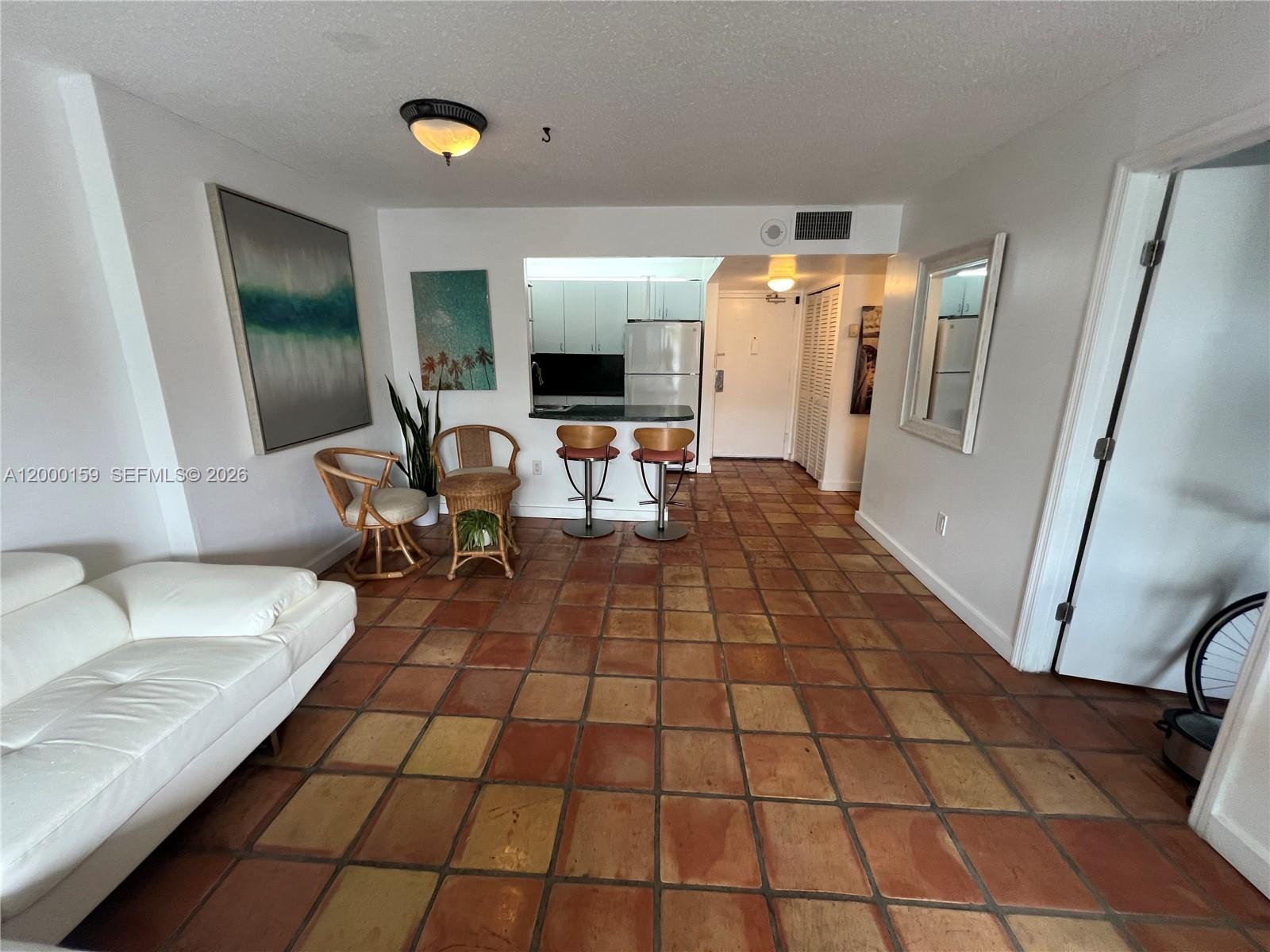 A living room with terracotta tile flooring features a white sofa and a kitchen pass-through — 345 Ocean Dr # 303, Miami Beach FL 33139, MIAMI BEACH, FL