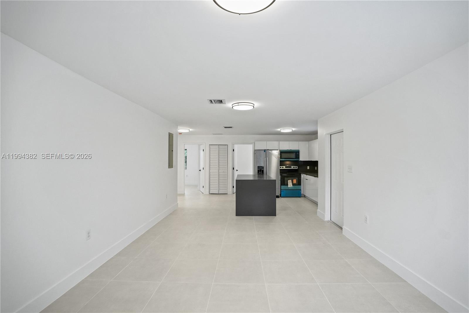 A kitchen with a dark island and white cabinets opens into a large tiled room — 5823 NW 30th ave # 5823, Miami FL 33142, MIAMI, FL