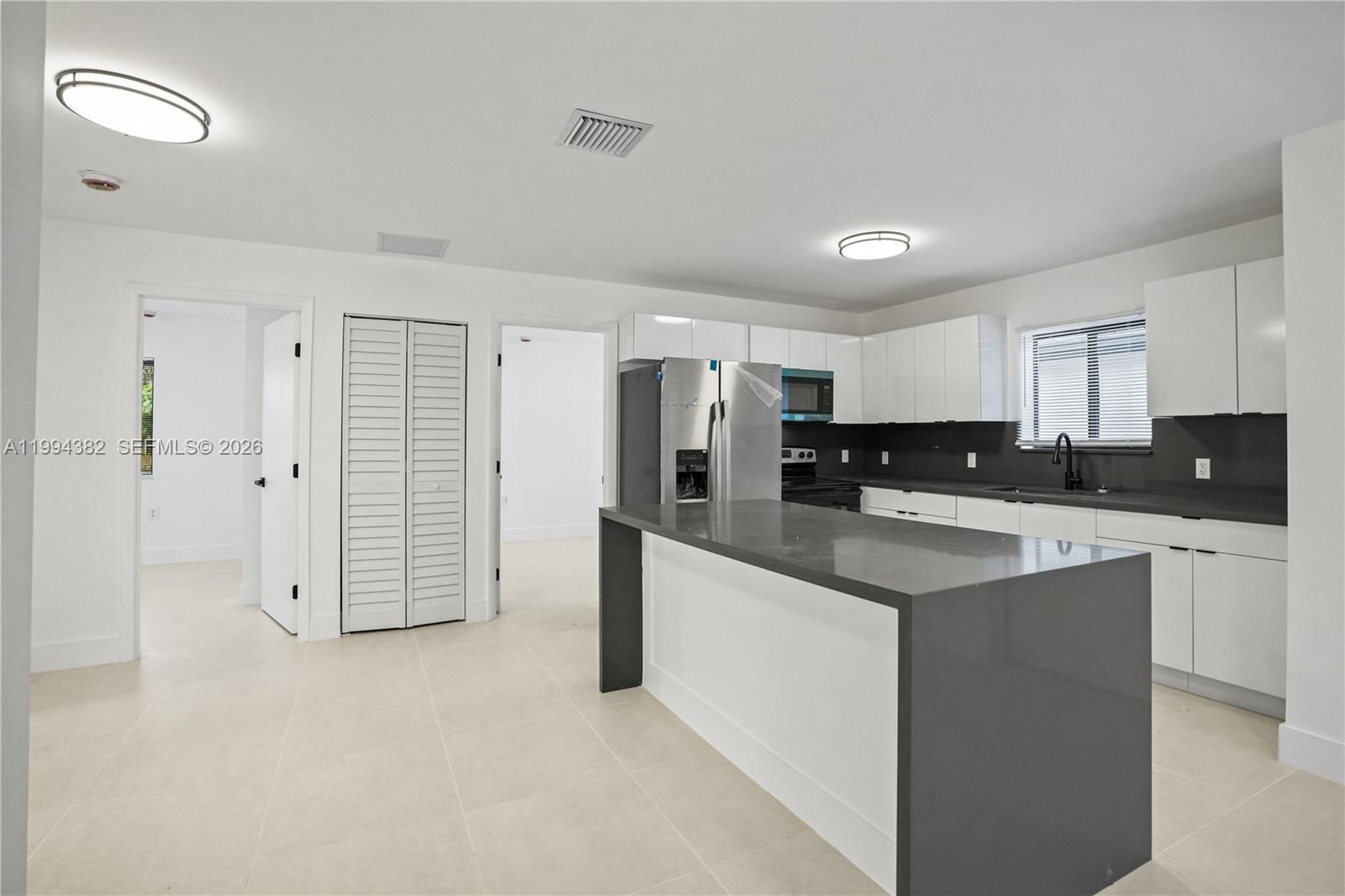 A modern kitchen features white cabinets, a dark gray island, and stainless steel appliances — 5823 NW 30th ave # 5823, Miami FL 33142, MIAMI, FL