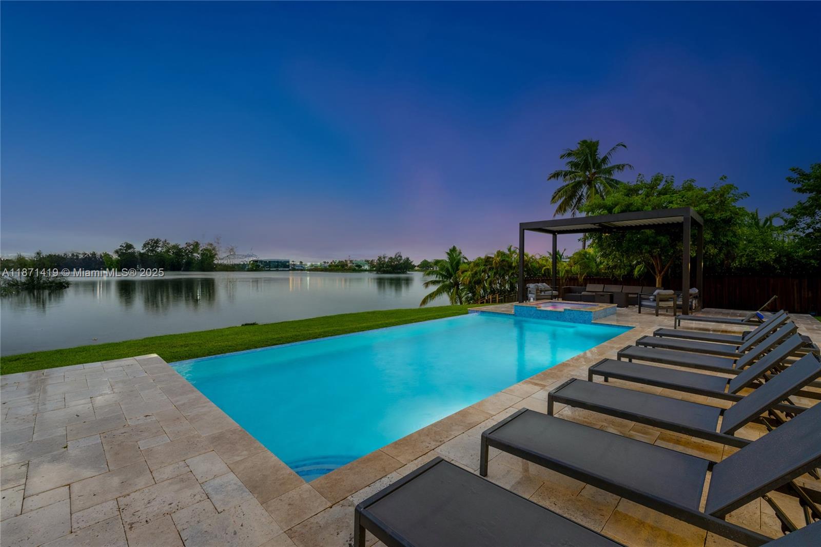 A swimming pool with lounge chairs sits on a patio overlooking a calm lake — 5420 SW 72nd Ave, Miami FL 33155, MIAMI, FL