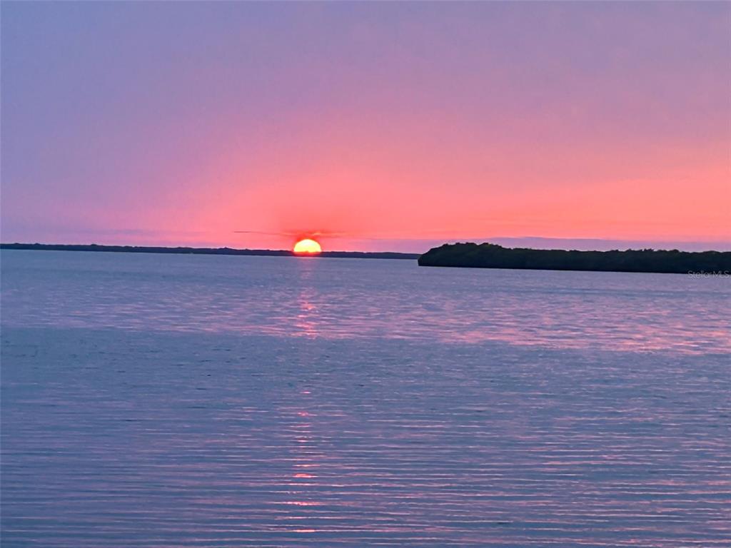 A vibrant sunset over a calm body of water with a distant shoreline — 1620 SEA BREEZE DRIVE, TARPON SPRINGS, FL