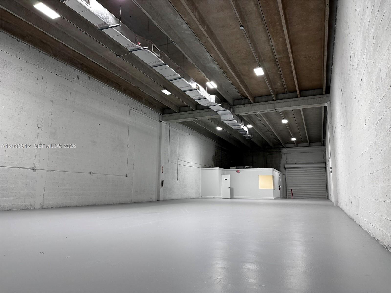 An empty industrial warehouse space features high ceilings, concrete walls, and a small office enclosure — FL