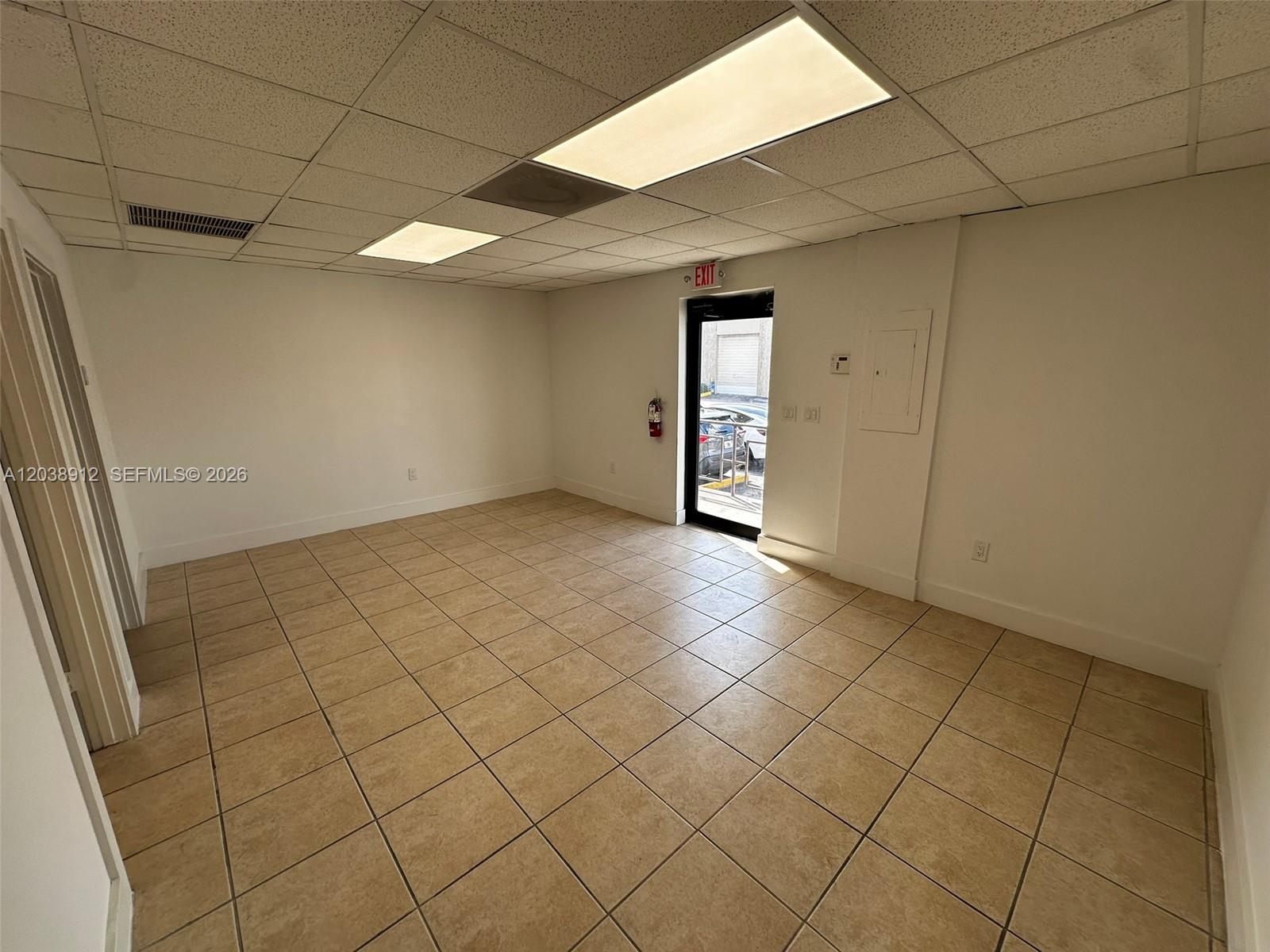 An empty office space features beige tile flooring, a drop ceiling, and a glass exit door — FL