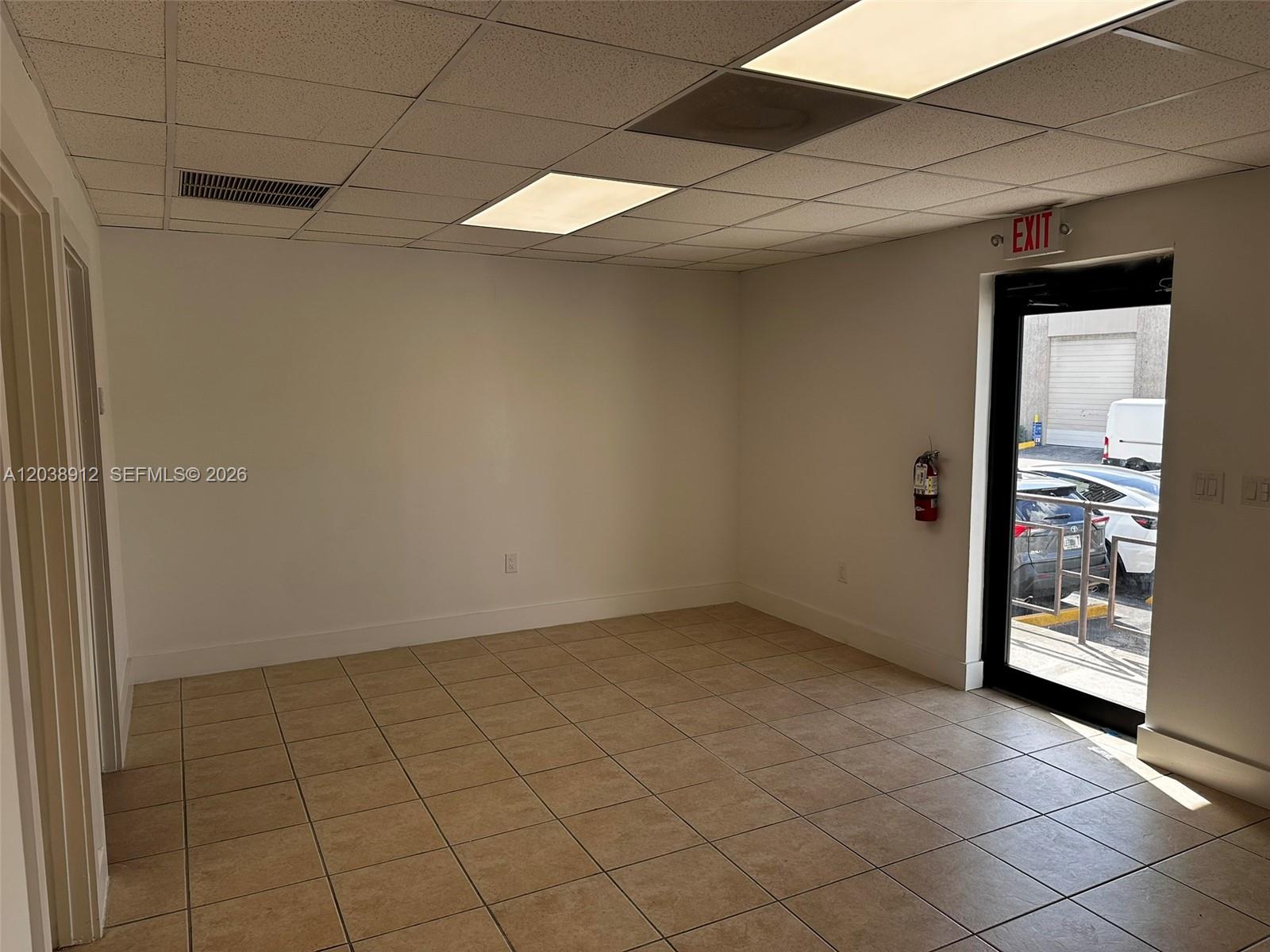 An empty office space with beige tile flooring, white walls, and a glass exit door — FL