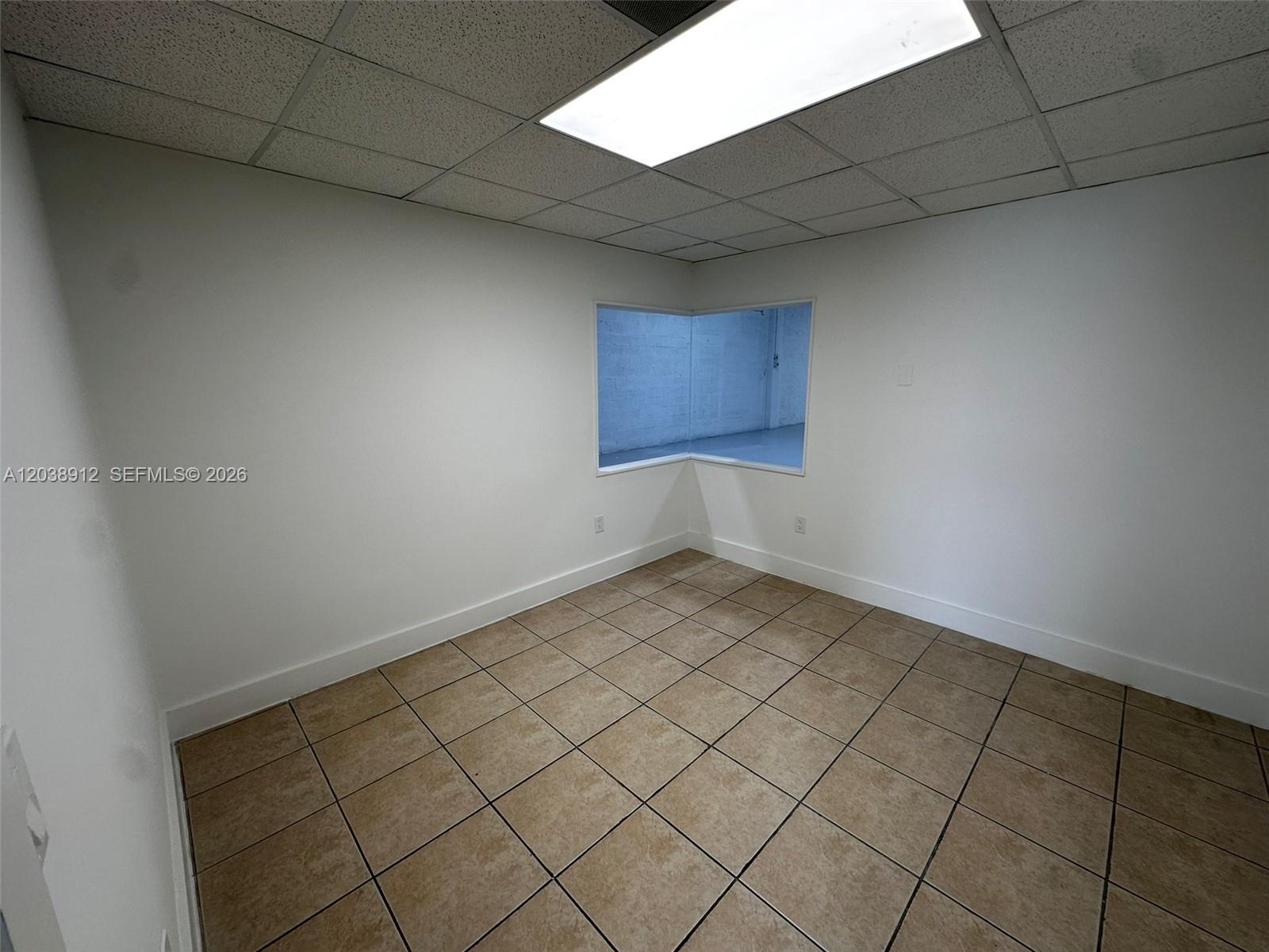 An empty room features white walls, tan tile flooring, and a corner window — FL