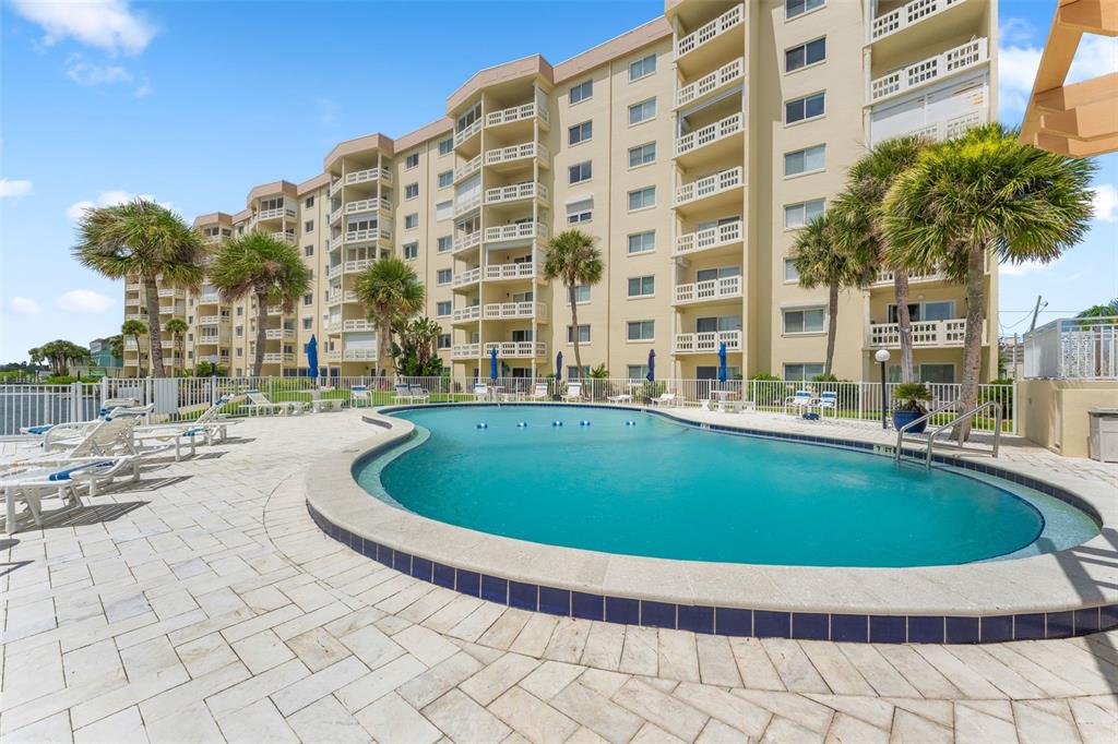A swimming pool sits on a paved patio in front of a multi-story apartment building — 3606 S PENINSULA DRIVE UNIT 102, PORT ORANGE, FL