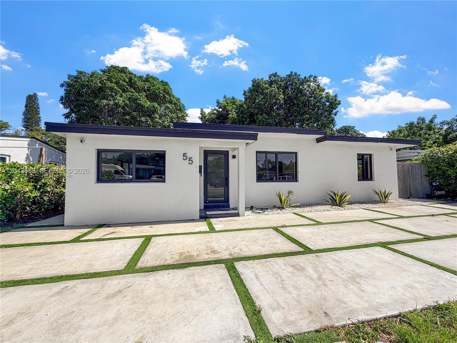 A single-story white house features a flat roof, dark-framed windows, and a concrete paver driveway — 55 NW 125th St, North Miami FL 33168, NORTH MIAMI, FL