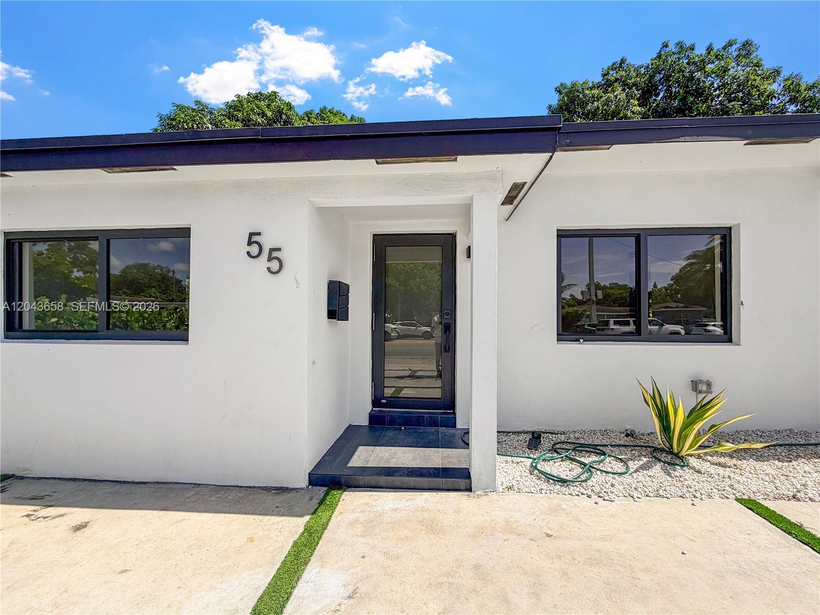 The exterior of a white house features a dark-framed glass door and two windows — 55 NW 125th St, North Miami FL 33168, NORTH MIAMI, FL