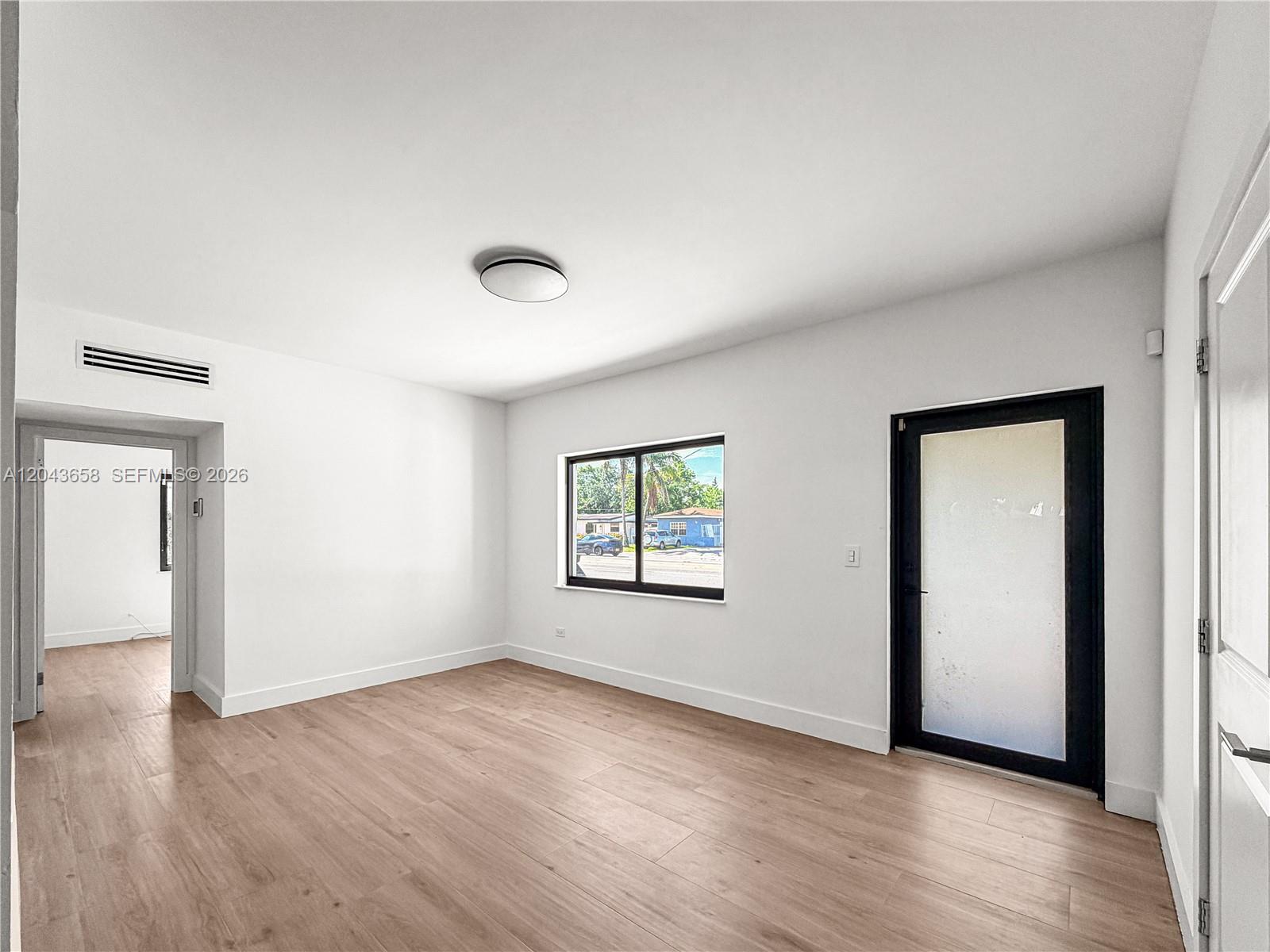 An empty room features light wood flooring, white walls, a window, and a glass-paneled door — 55 NW 125th St, North Miami FL 33168, NORTH MIAMI, FL