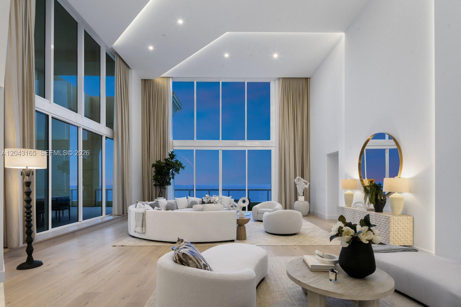 A spacious living room features floor-to-ceiling windows, white curved furniture, and light wood flooring — 17875 Collins Ave, Sunny Isles Beach FL 33160, SUNNY ISLES BEACH, FL