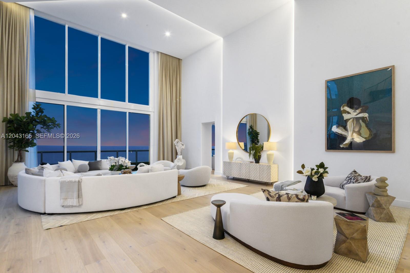 A spacious living room features high ceilings, floor-to-ceiling windows, and modern white curved furniture — 17875 Collins Ave, Sunny Isles Beach FL 33160, SUNNY ISLES BEACH, FL
