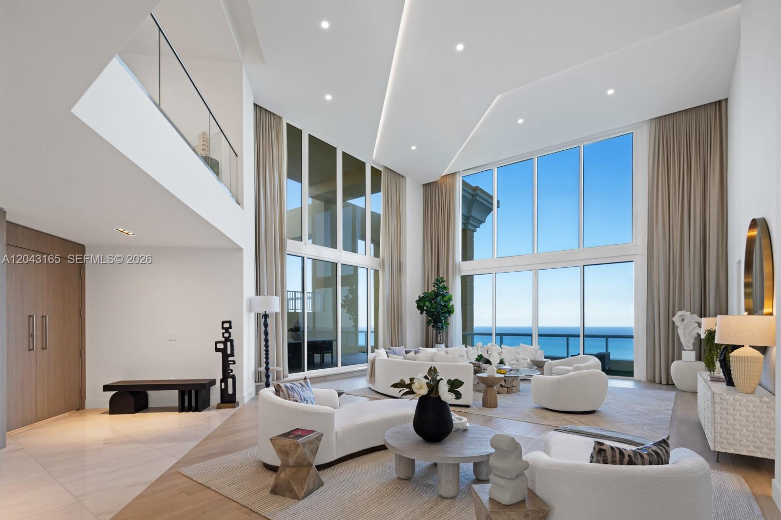 A spacious living room features double-height ceilings, floor-to-ceiling windows, and panoramic ocean views — 17875 Collins Ave, Sunny Isles Beach FL 33160, SUNNY ISLES BEACH, FL