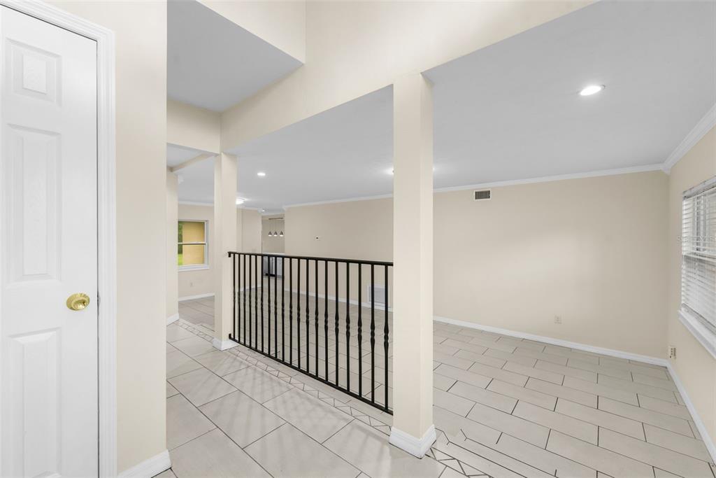 An interior view of a room with light-colored tile flooring and a black metal railing — 10907 SW 24TH AVENUE, GAINESVILLE, FL