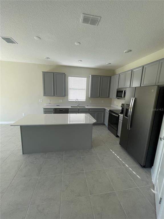A kitchen features gray cabinets, white countertops, a center island, and stainless steel appliances — 4491 TAHOE CIRCLE, CLERMONT, FL