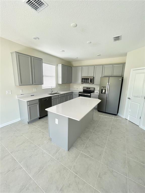 A kitchen features gray cabinets, white countertops, a center island, and stainless steel appliances — 4491 TAHOE CIRCLE, CLERMONT, FL