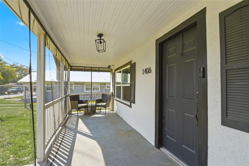 A covered front porch features a dark door, a light fixture, and two outdoor chairs — 1406 W 15TH STREET, SANFORD, FL