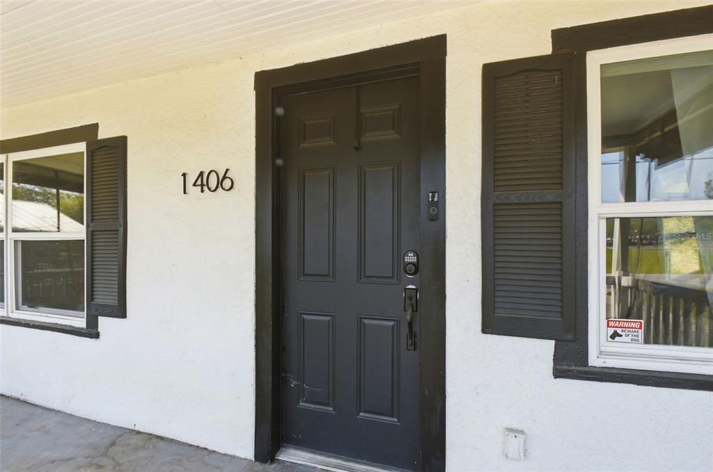 A black front door with a digital lock sits between two windows with black shutters — 1406 W 15TH STREET, SANFORD, FL
