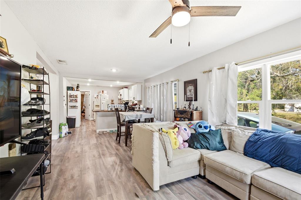 An open-concept living room and kitchen feature light wood-look flooring and a ceiling fan — 1406 W 15TH STREET, SANFORD, FL