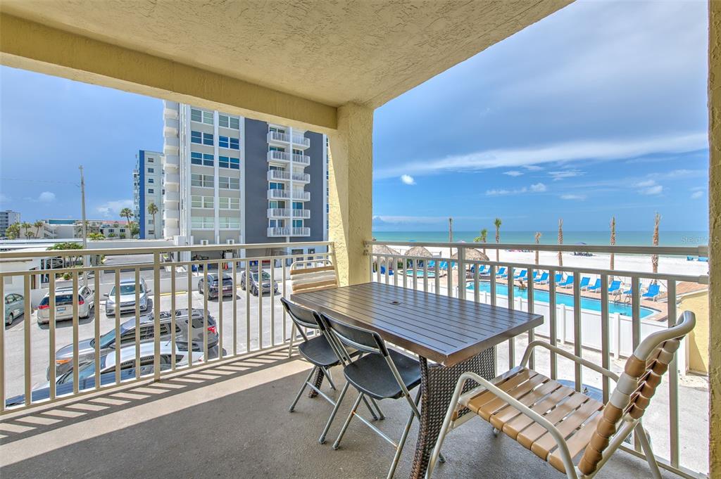 A balcony with a dining table and chairs overlooks a parking lot, swimming pool, and beach — 17450 GULF BOULEVARD UNIT 103, REDINGTON SHORES, FL