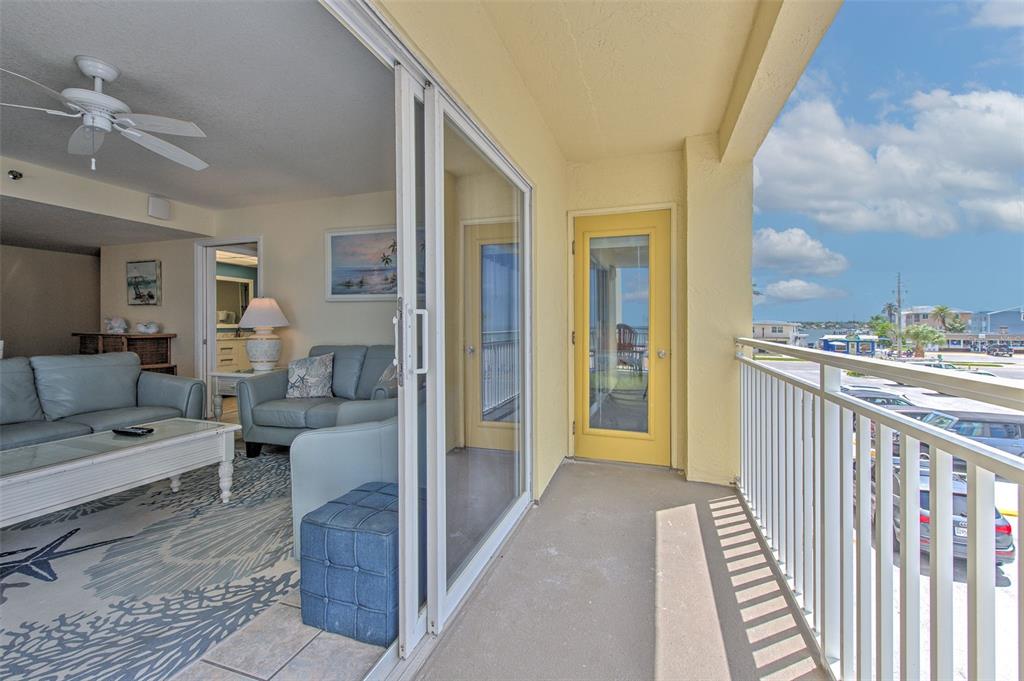 A balcony with a yellow door overlooks a parking lot and water under a blue sky — 17450 GULF BOULEVARD UNIT 103, REDINGTON SHORES, FL