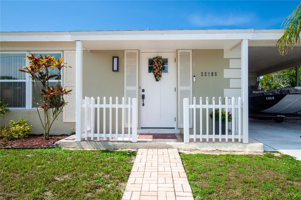 A white front door with a wreath is centered between white picket fences and shutters — 22295 MONTROSE AVENUE, PORT CHARLOTTE, FL