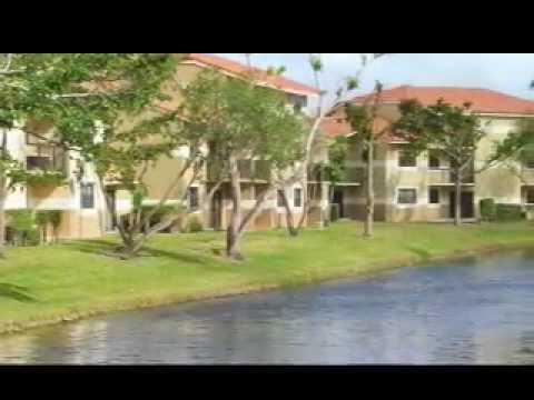 A multi-story apartment complex sits behind a grassy lawn and a small canal — SUNRISE, FL