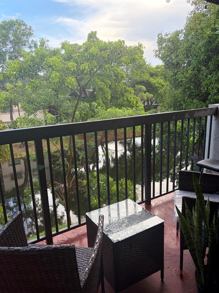 A balcony with wicker furniture overlooks a small pond surrounded by lush green trees — SUNRISE, FL