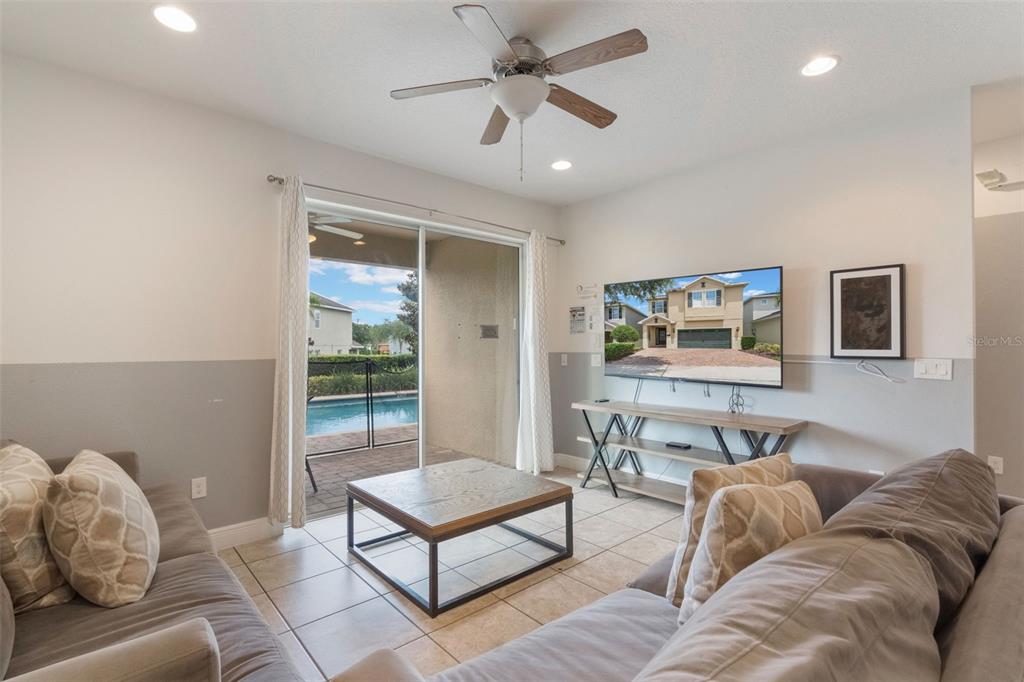 A living room with tile floors, a ceiling fan, a television, and a sliding glass door — 331 PENDANT COURT, KISSIMMEE, FL