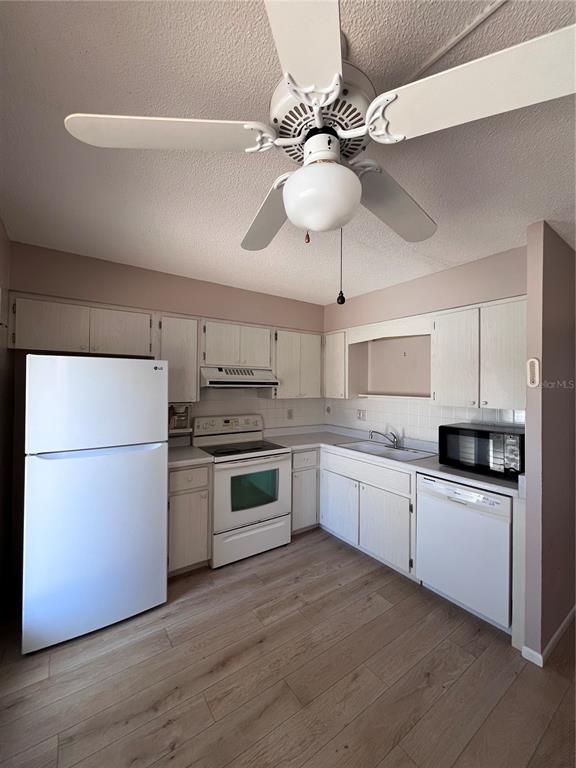 A kitchen features white appliances, light wood-look flooring, and white cabinets with a ceiling fan — 509 W VENICE AVENUE UNIT 102, VENICE, FL