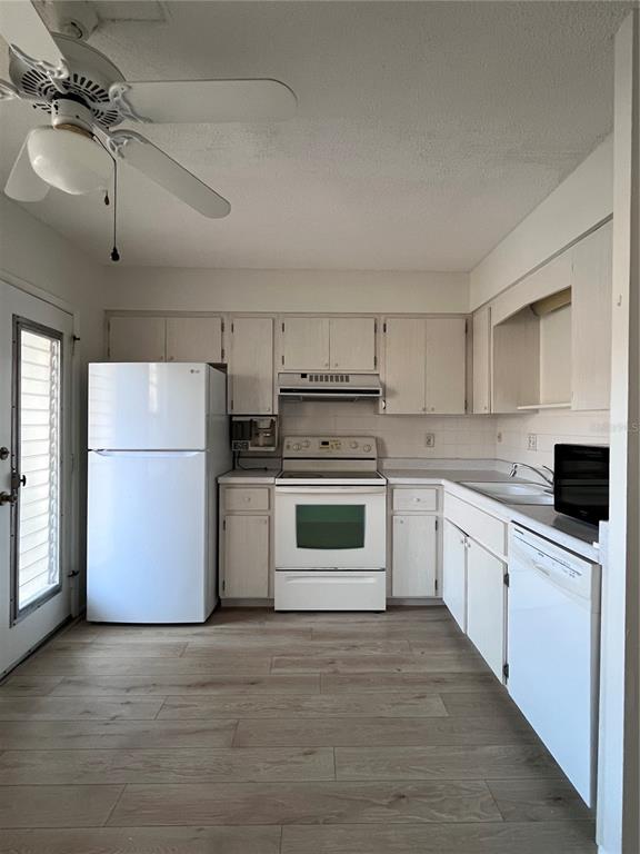 A kitchen with white appliances, light wood-look flooring, and off-white cabinets — 509 W VENICE AVENUE UNIT 102, VENICE, FL