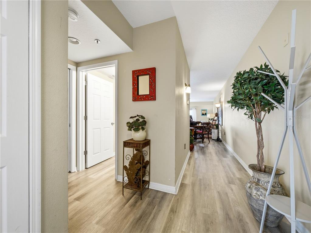 A hallway with light wood-look flooring leads to a dining area with a potted tree — 5300 S ATLANTIC AVENUE UNIT 3-302, NEW SMYRNA BEACH, FL